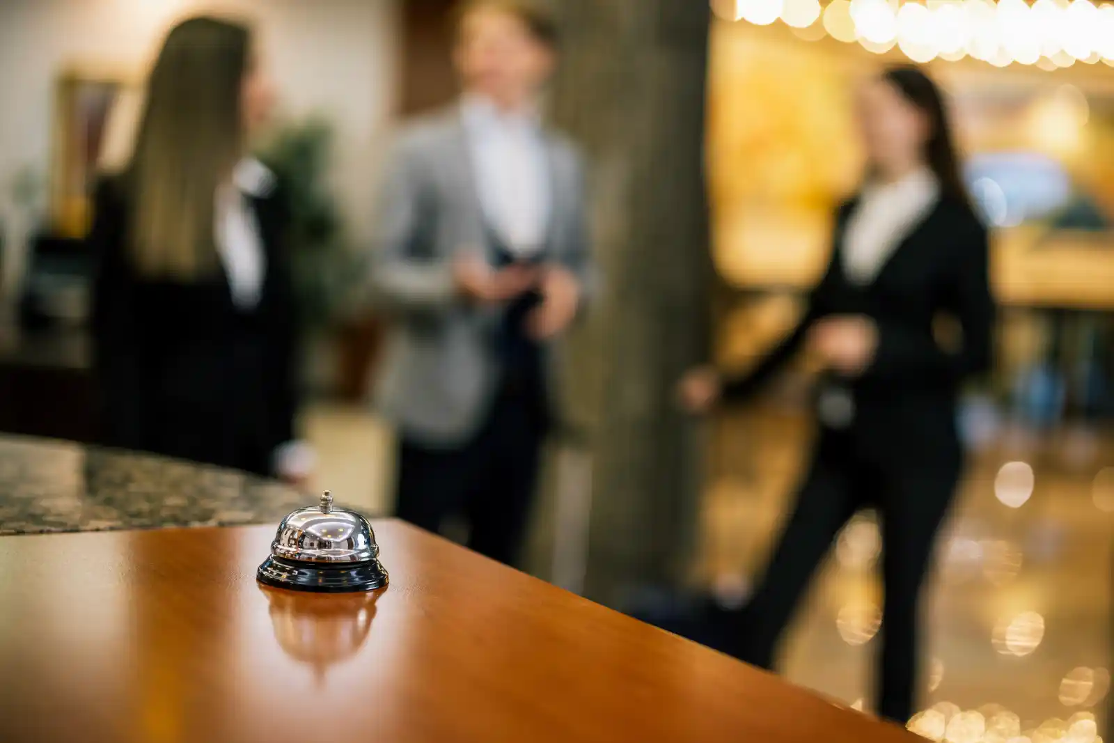 Conciergerie de luxe : cloche de réception sur le comptoir d’un palace, concierges en arrière-plan