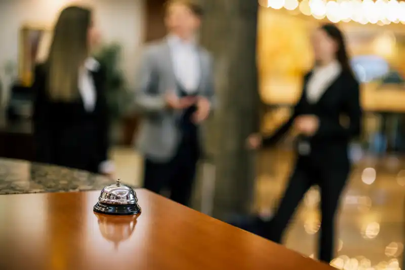 Conciergerie de luxe : cloche de réception sur le comptoir d’un palace, concierges en arrière-plan